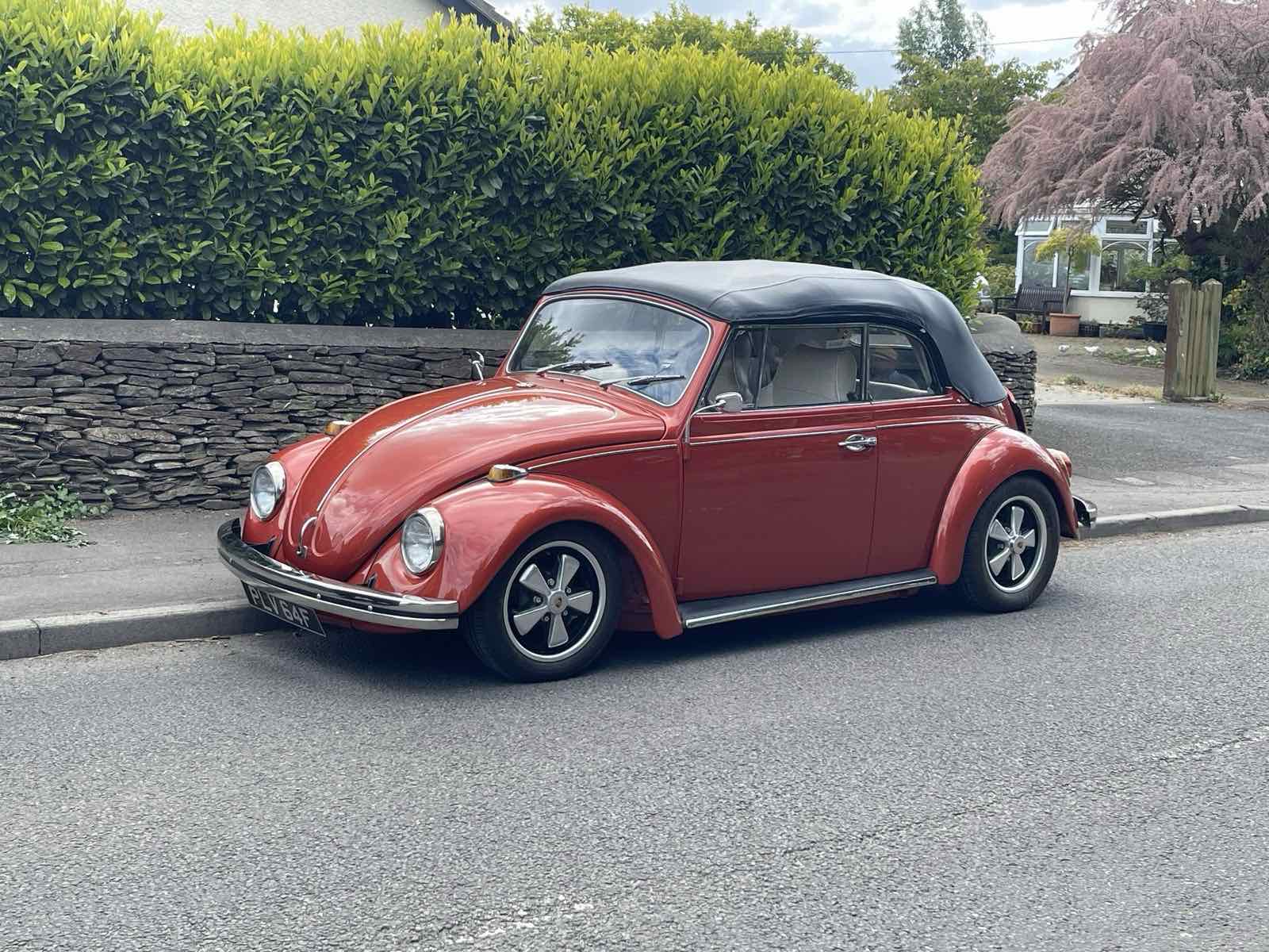 A red VW Beetle cabriolet with a black hood parked on a street