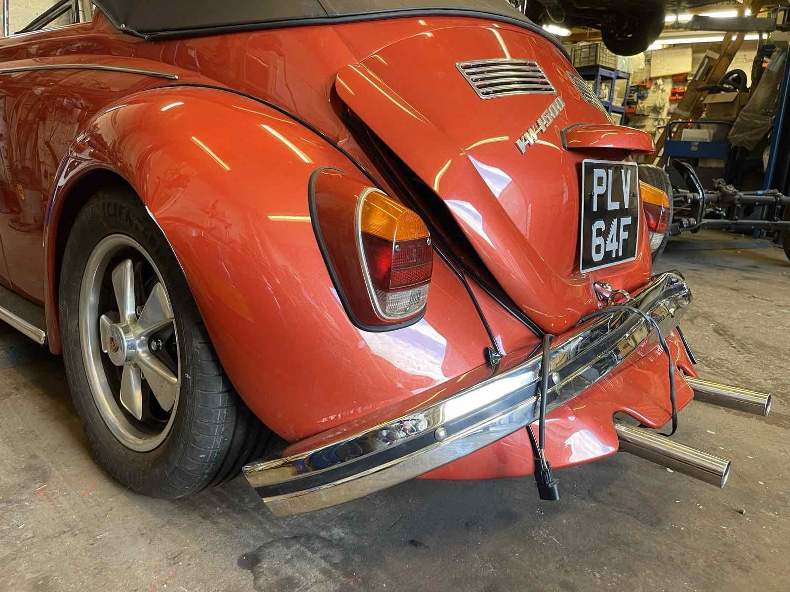 The rear of a red Beetle cabriolet with twin exhaust tips, in the workshop
