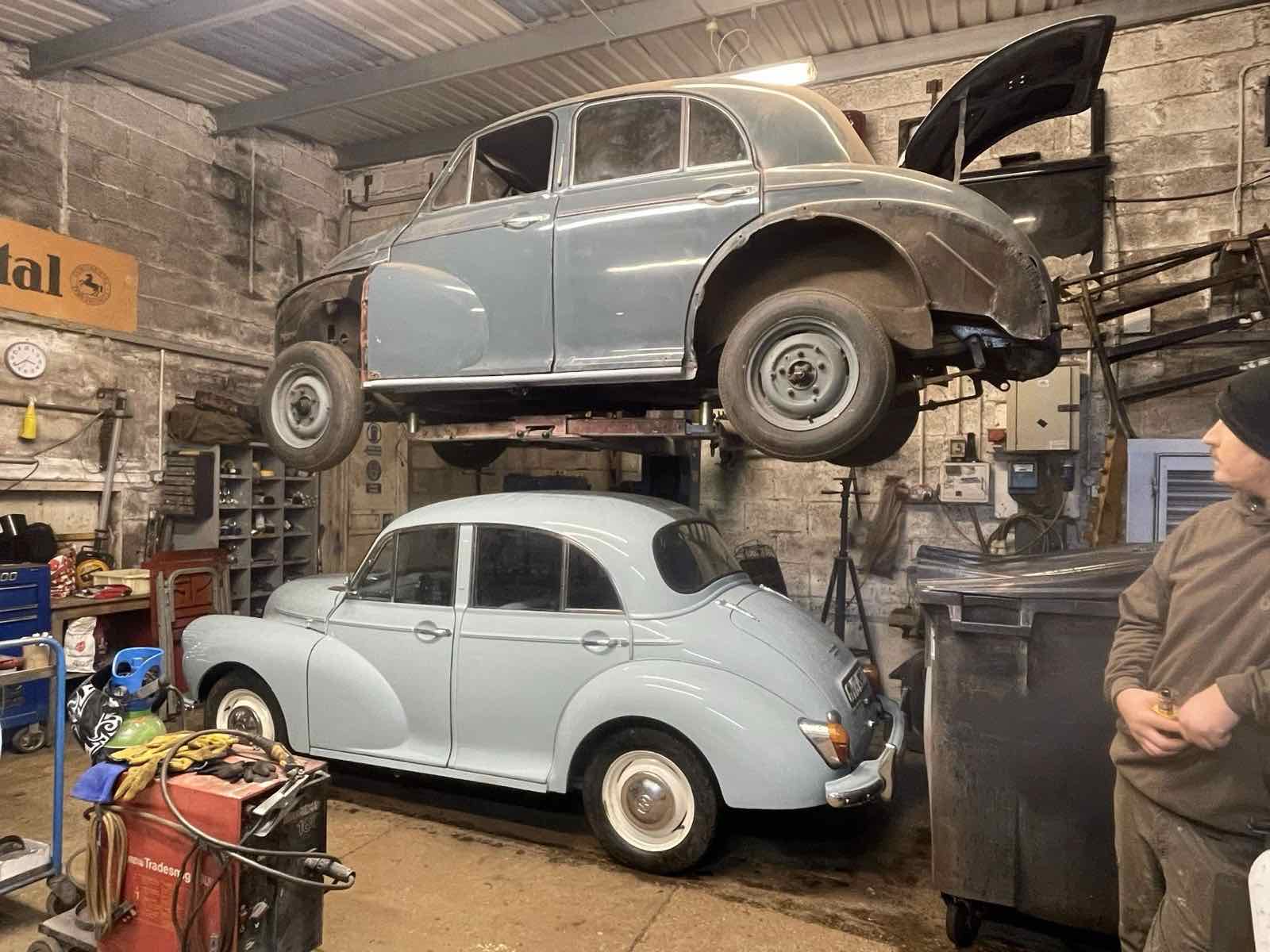 A blue Morris Minor up on the lift above another blue Morris Minor