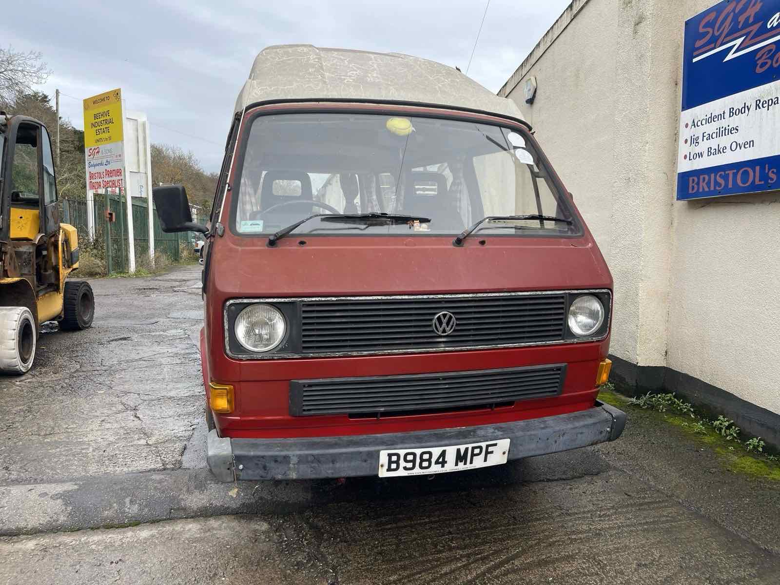 A red VW T25 high-top camper in the yard